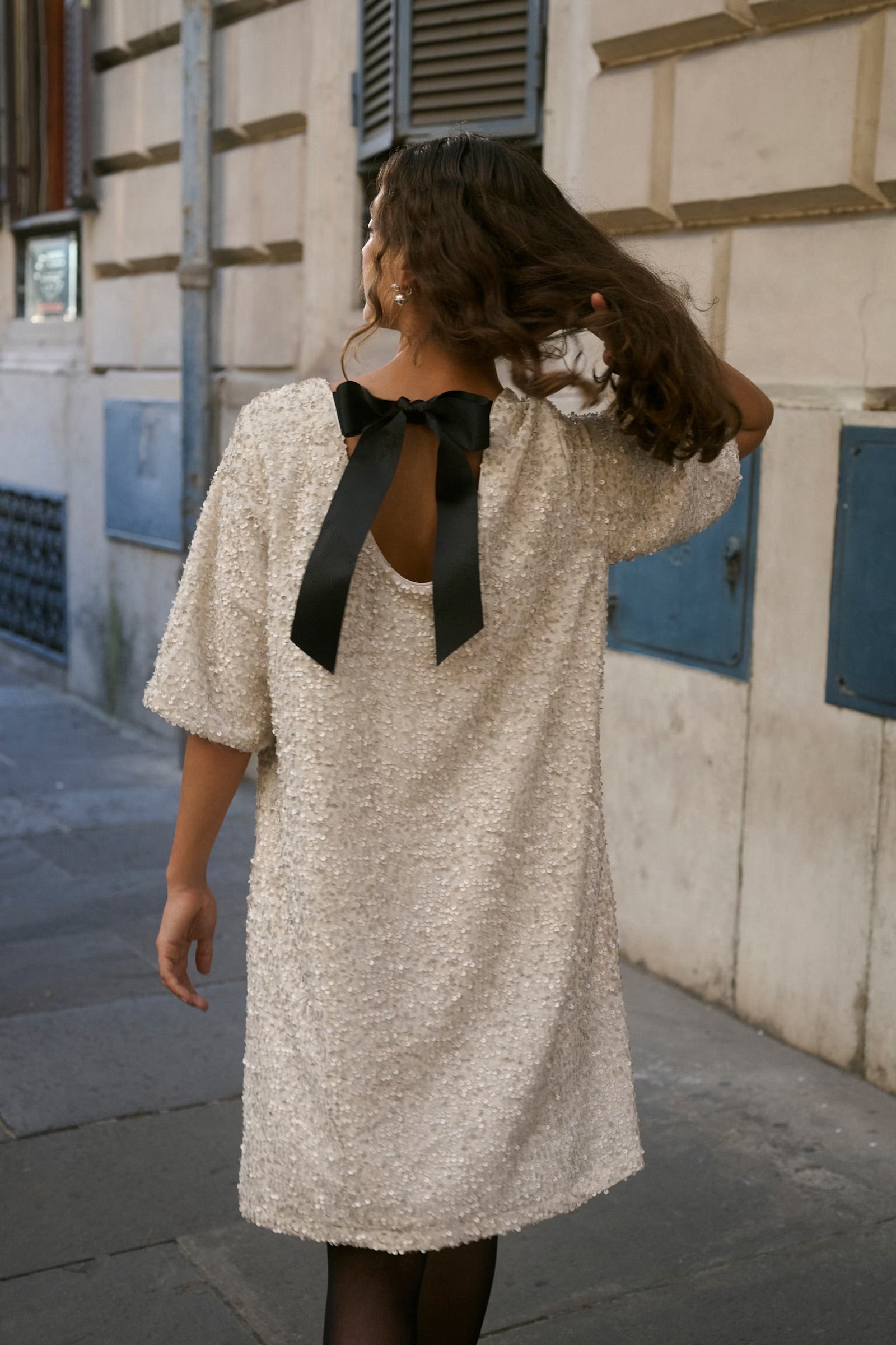 Woman wearing a textured dress with a black bow detail, walking on a street.
